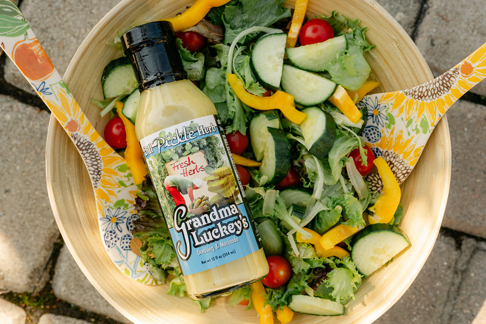 Bowl of salad with a bottle of 'Grandma Lucky's' dill pickle herb salad dressing on a stone surface