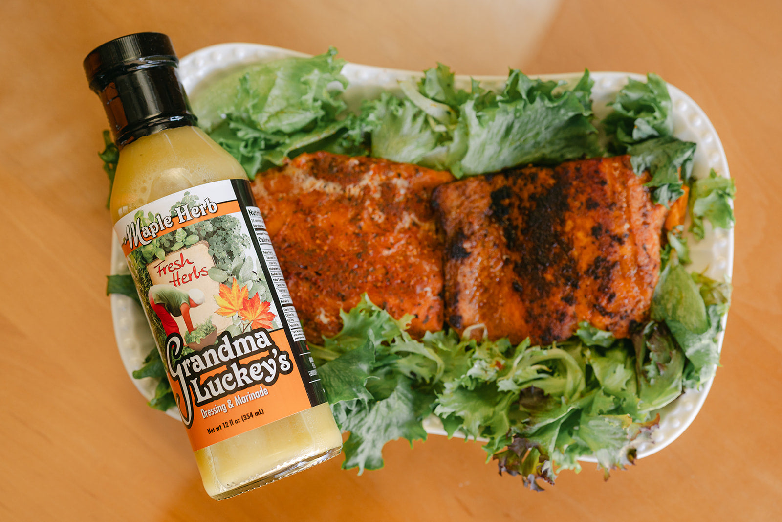 Salmon dish with lettuce and a bottle of Grandma Luckey's dressing Maple Herb on a wooden surface
